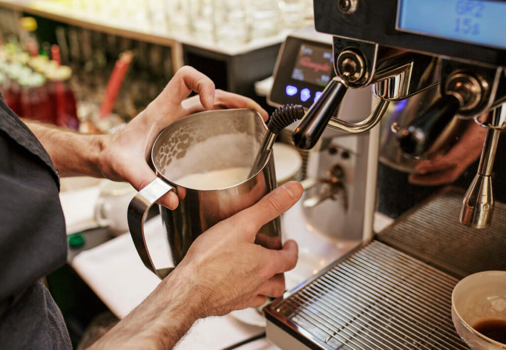 barista našlehává mléko za pomoci profesionálního kávovaru